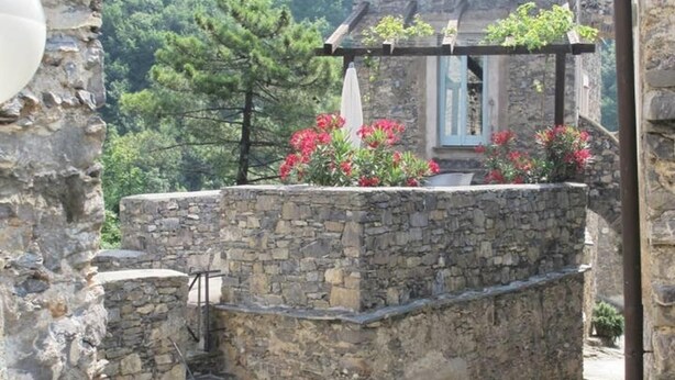 Un edificio de piedra con una pérgola de madera y flores rojas.