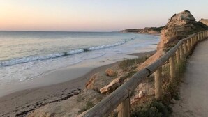 A coastal walkway with a wooden railing, leading to a beach with gentle waves and a rocky cliff in the background. - PORT WILLUNGA DREAMING a beach front experience (Port Willunga)