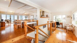A spacious living area with wooden flooring, a dining area, and large windows offering views. - PORT WILLUNGA DREAMING a beach front experience (Port Willunga)