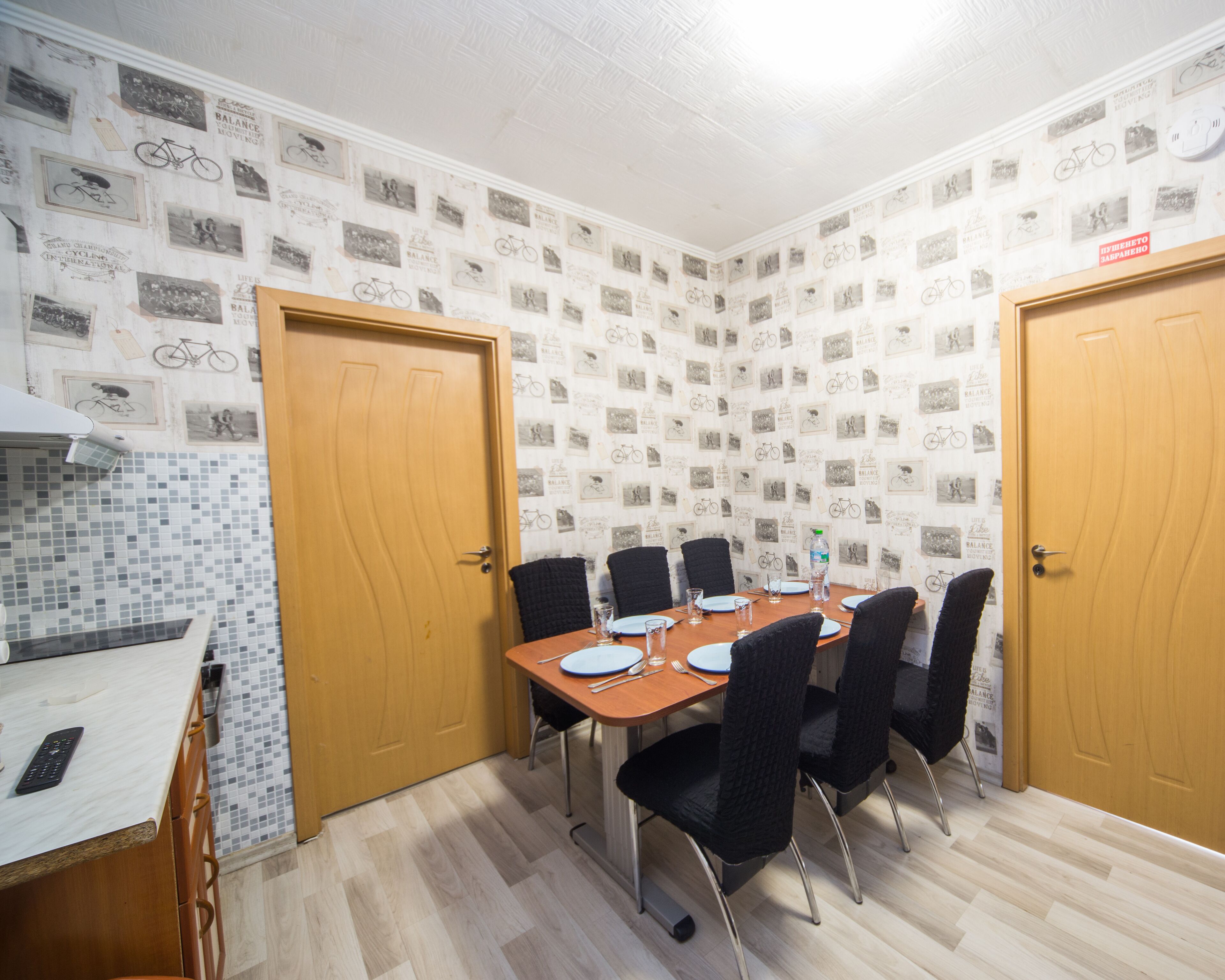 A dining room with a wooden table set for four, surrounded by black chairs. The room features a tiled backsplash with bicycle-themed decorations and two wooden doors.