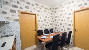 Ein Esszimmer mit einem Holztisch, gedeckt für vier Personen, umgeben von schwarzen Stühlen. Der Raum verfügt über eine geflieste Spritzschutzleiste mit Fahrradmotiven und zwei Holztüren.