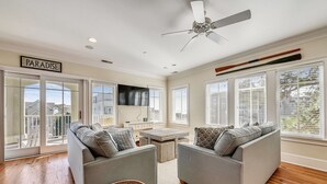 A spacious living room with two grey sofas, a ceiling fan, a flat-screen TV, and large windows with blinds. - Fantastic Pet Friendly Multi Family Home w/ Pool (Hilton Head Island)