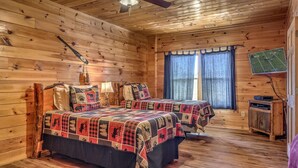 Une chambre de type cabine avec deux lits, un ventilateur de plafond, une fenêtre avec des rideaux et un téléviseur fixé au mur.