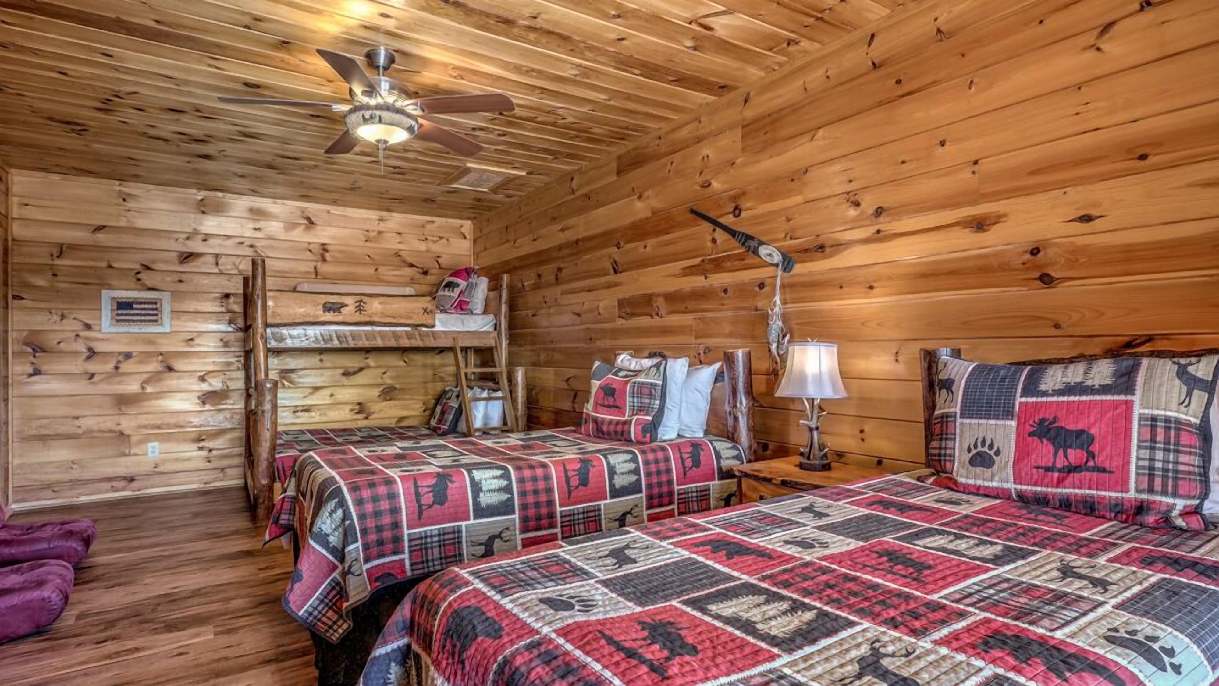 A cabin with two beds, wooden walls, a ceiling fan, and a small table with a lamp.