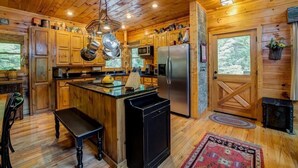 Une cuisine rustique, située dans une cabane en bois, avec un îlot central, des appareils en acier inoxydable et une grande fenêtre.
