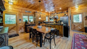 A wooden cabin with a dining area, kitchen, and large windows.