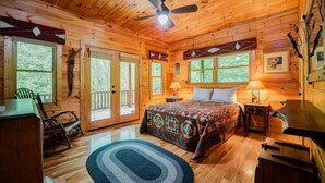 Une chambre située dans une cabane en rondins, avec un lit, un bureau, une chaise et un ventilateur de plafond.