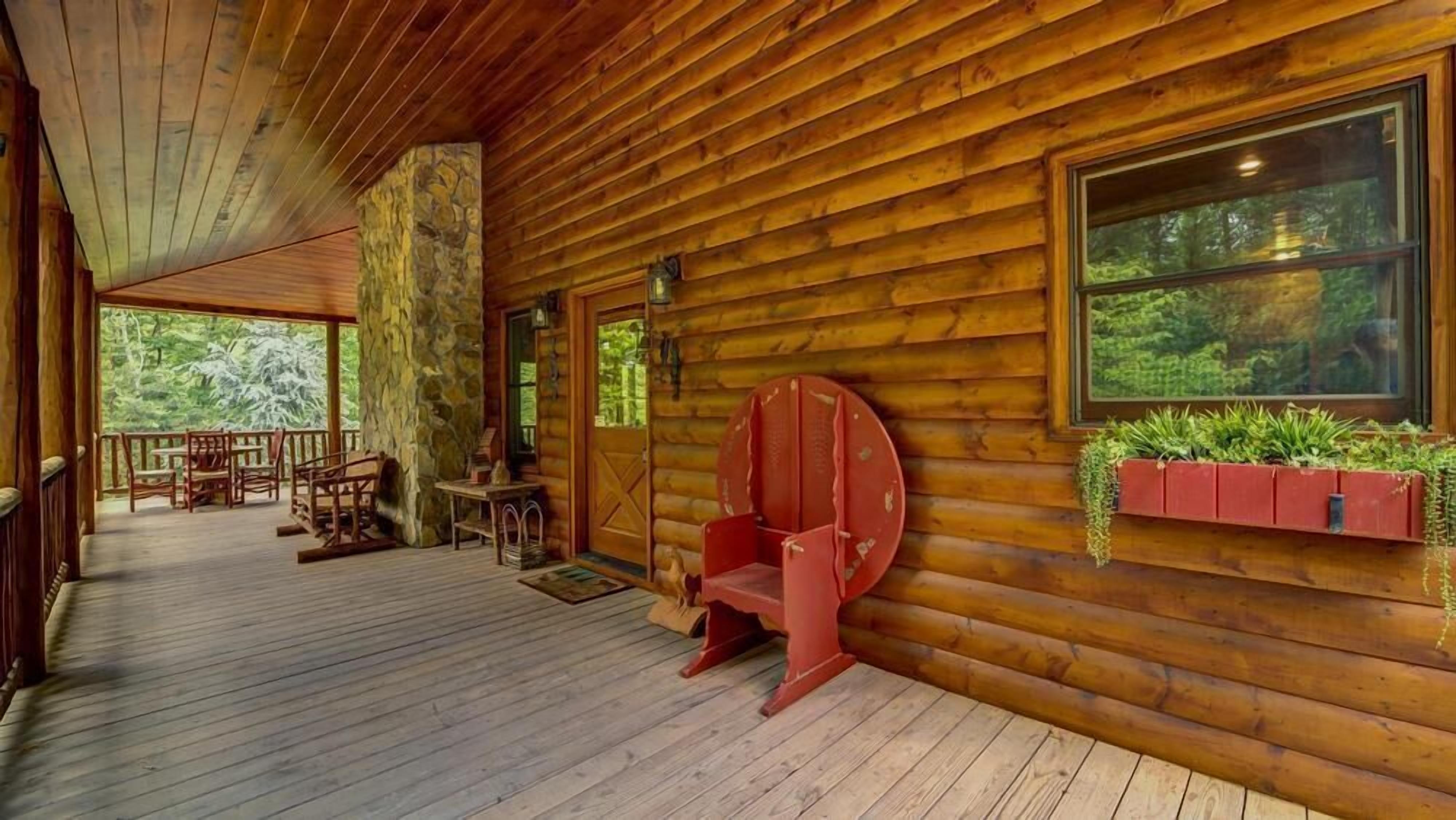 A wooden cabin with a porch, stone wall, and a window with plants.