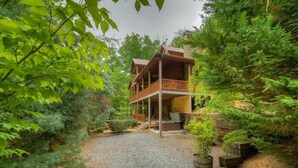 Une cabane en bois dotée d’un porche et d’une allée en gravier, le tout entouré d’une végétation luxuriante.