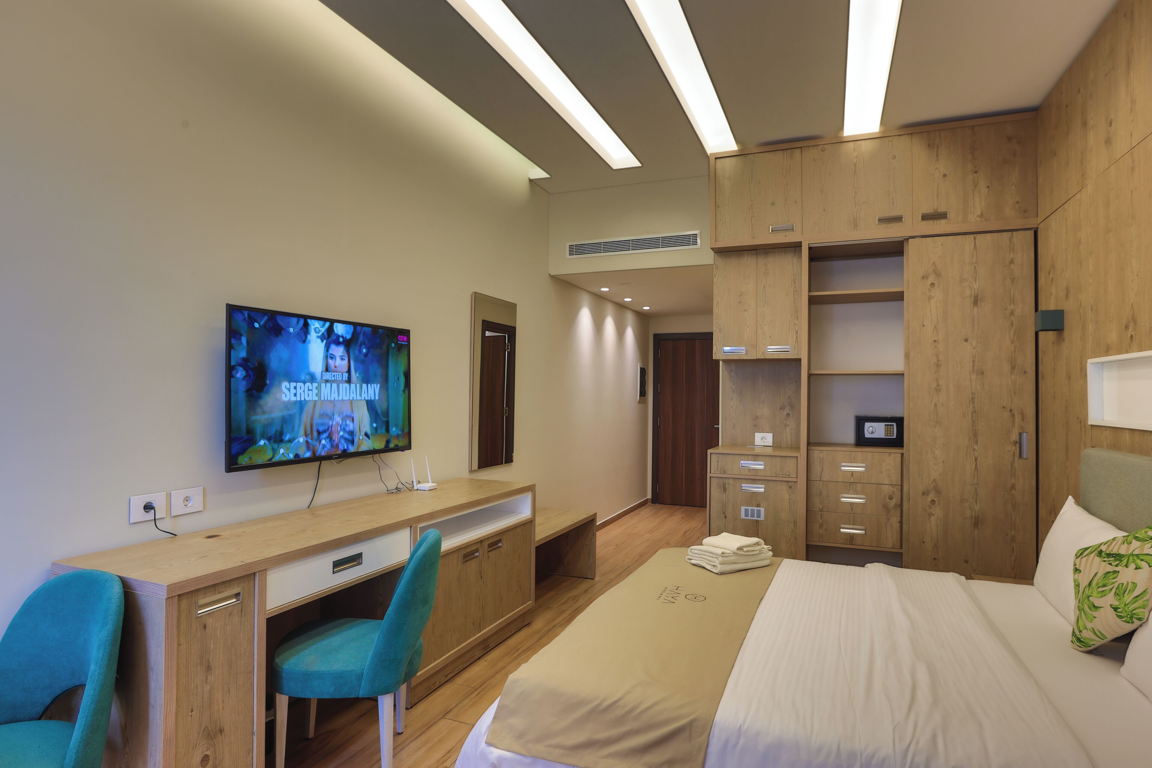 Una habitación de hotel moderna con una cama, un escritorio con computadora, un televisor y muebles de madera.