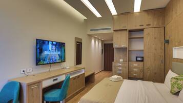 Una habitación de hotel moderna con una cama, un escritorio con computadora, un televisor y muebles de madera.