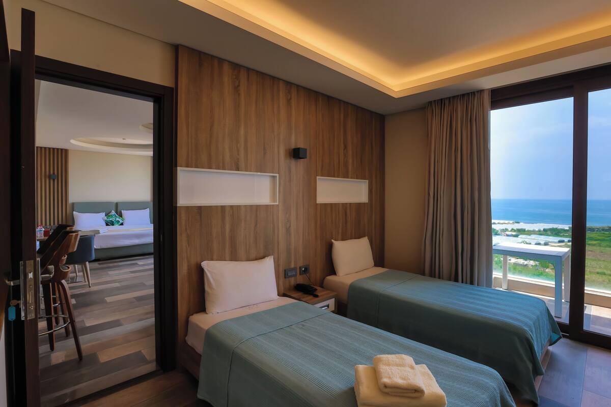 A hotel room with two beds, a desk, and a view of the sea.