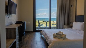 A modern hotel room with a large bed, a desk, a TV, and a balcony with a view of the beach. - Haya hotel & spa (Tabarja)