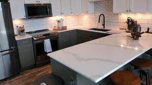 Une cuisine moderne avec des meubles blancs, un réfrigérateur en acier inoxydable, un four à micro-ondes et une machine à café.
