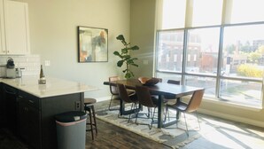 Une cuisine moderne dotée d’un grand îlot central, d’un coin repas avec des chaises et offrant une vue sur la ville grâce à de grandes fenêtres.