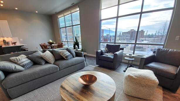 Un salon moderne avec un canapé gris, une table basse ronde et une grande fenêtre donnant sur la ville.