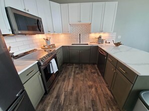 Una cocina moderna con armarios blancos, estufa de acero inoxidable y microondas.