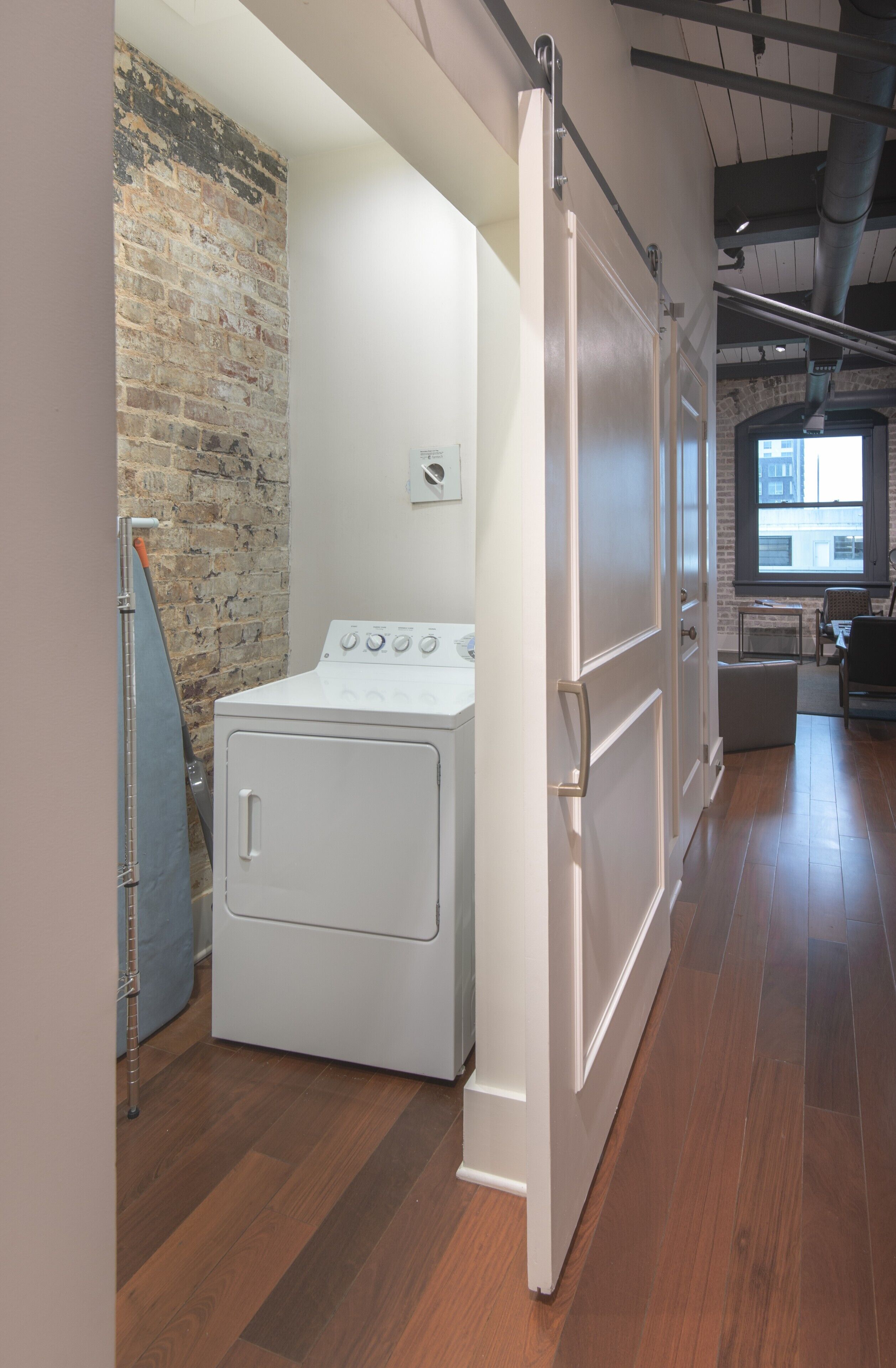 A laundry room with a white washer and dryer, a brick wall, and a large window.