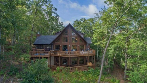 A large wooden cabin with multiple decks and large windows, surrounded by dense forest. - Above and Beyond- Pet Friendly | Screened Porch | Outdoor Fireplace (Blue Ridge)