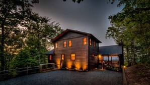 A two-story log cabin with a porch and a small deck, surrounded by trees. - Above and Beyond- Pet Friendly | Screened Porch | Outdoor Fireplace (Blue Ridge)