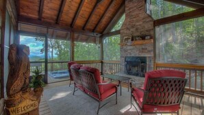 A wooden deck with two red chairs, a stone fireplace, and a 'Welcome' sign. - Above and Beyond- Pet Friendly | Screened Porch | Outdoor Fireplace (Blue Ridge)