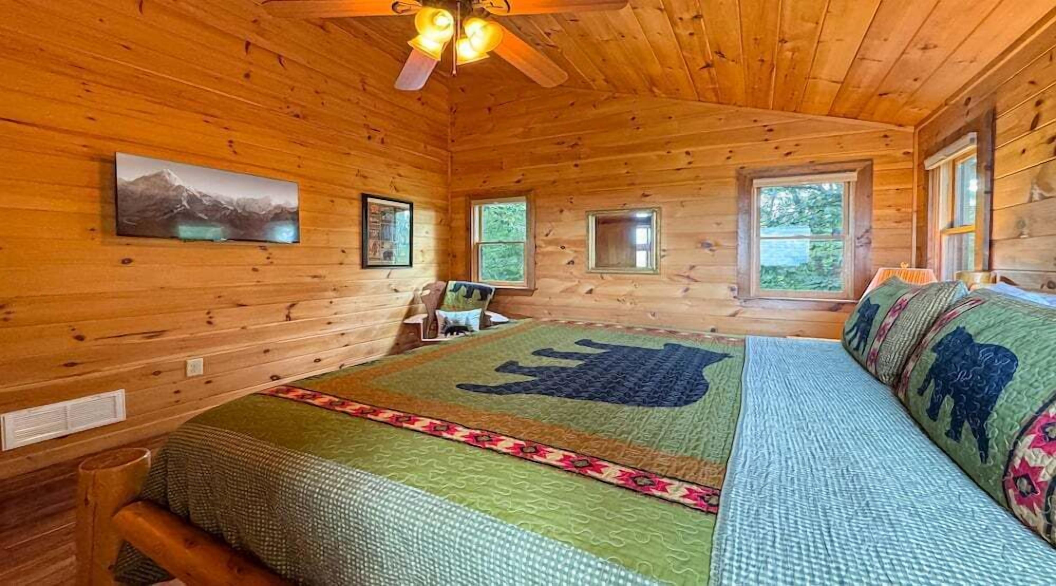 A log cabin bedroom with a bed, a ceiling fan, and a mountain painting on the wall.