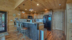 A wooden cabin kitchen with a central island, bar stools, a stainless steel refrigerator, and wooden cabinets. - Above and Beyond- Pet Friendly | Screened Porch | Outdoor Fireplace (Blue Ridge)