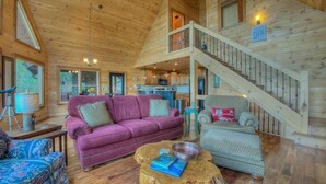 A cozy cabin interior with a wooden staircase, a purple sofa, and a dining area. - Above and Beyond- Pet Friendly | Screened Porch | Outdoor Fireplace (Blue Ridge)