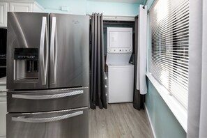Un refrigerador de acero inoxidable con dispensador de agua, una lavadora y una ventana con persianas.