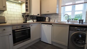 A compact kitchen with white cabinets, a microwave, a kettle, a dishwasher, and a washing machine. - Woodlands View (Halesworth)