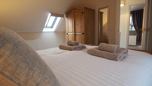 A bedroom with a large bed, a wooden wardrobe, a skylight, and a view of the hallway. - Woodlands View (Halesworth)