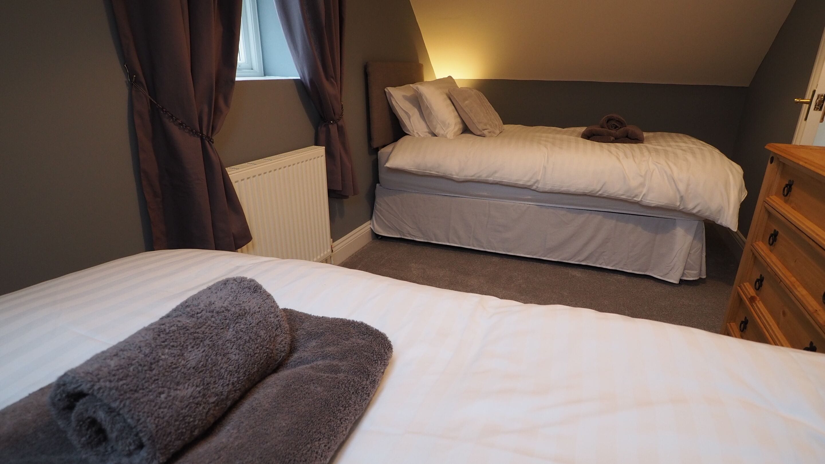 Une chambre avec deux lits, une commode et un radiateur.