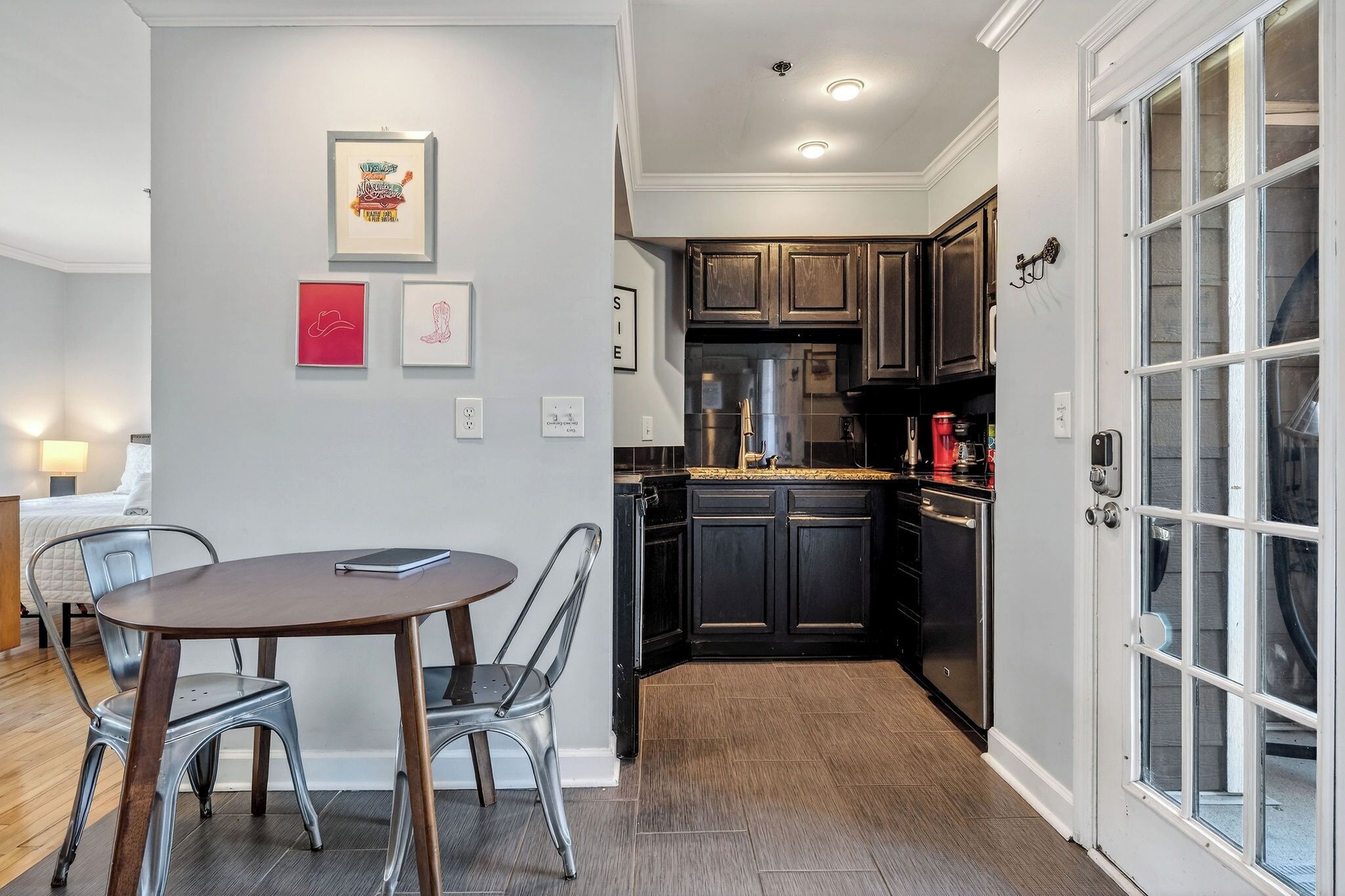 A modern kitchen with dark cabinetry, a dining area with a round table and metal chairs, and a large window with a view.