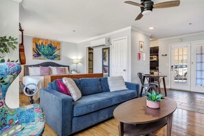 A living room with a blue sofa, a round table, a guitar, and a ceiling fan.