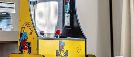 A Pac-Man arcade machine on a table with a pink chair in the foreground.