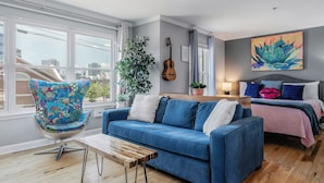 Ein modernes Wohnzimmer mit einem blauen Sofa, einem farbenfrohen Sessel, einem Holztisch, einer Gitarre und einem großen Gemälde an der Wand.