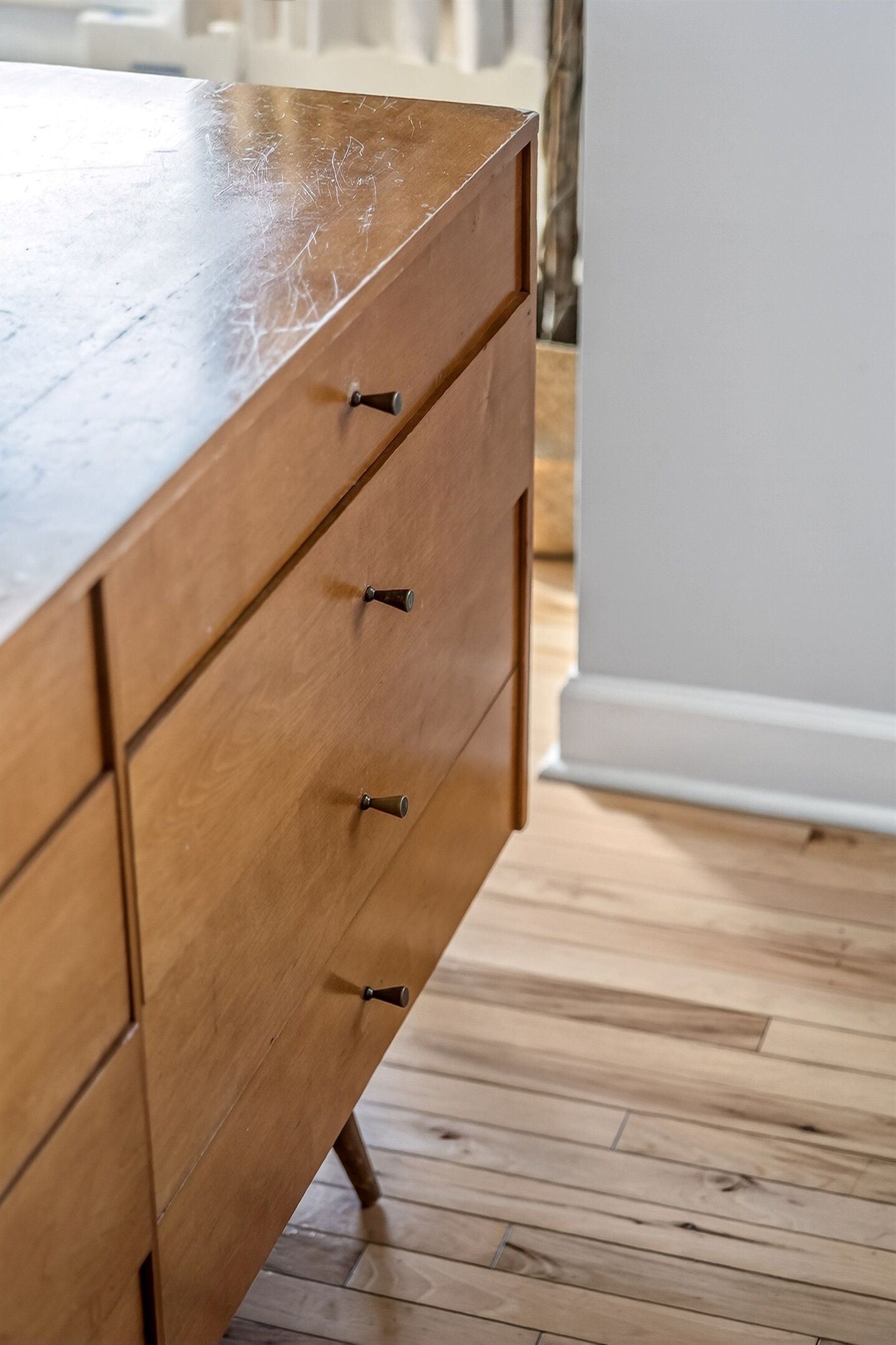 A wooden dresser with drawers and knobs, a white wall, and a wooden floor.