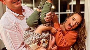 Une personne tenant un enfant dans une pièce avec une fenêtre et une porte en arrière-plan.