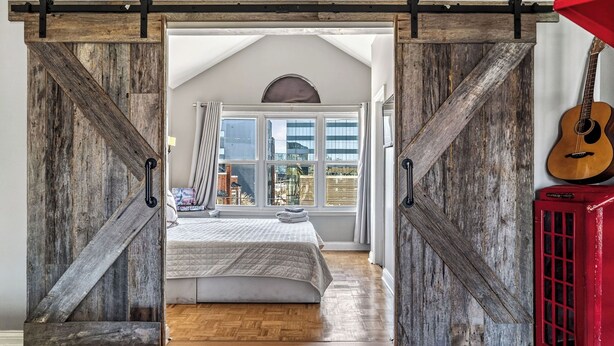 Un dormitorio con cama, piso de madera y vista por una ventana grande.