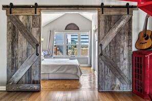 Een slaapkamer met een bed, houten vloer en uitzicht door een groot raam.