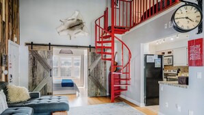 Una sala de estar moderna con un sofá azul, una mesa de centro de madera y una escalera espiral roja que conduce a un nivel superior.