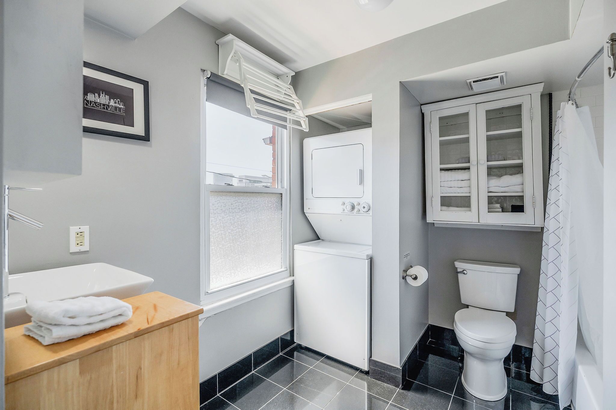 Une salle de bain moderne avec un lavabo blanc, un lave-linge encastré, des toilettes et un meuble avec des portes en verre.