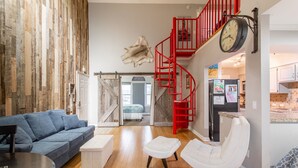 Amplia sala de estar con un sofá azul, un reposapiés blanco y una silla blanca. Una escalera espiral roja conduce a un nivel superior.