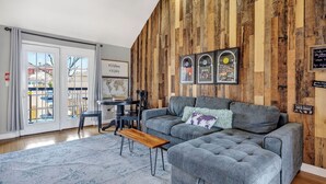Una sala de estar moderna con un sofá gris, paneles de madera, una mesa de comedor con sillas y un ventanal grande.