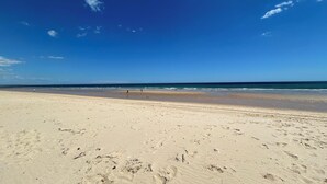 A wide sandy beach with footprints and a clear blue sky.