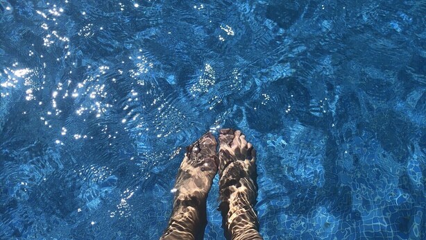 A person's legs in a swimming pool with clear water and visible ripples.