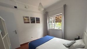 A bedroom with a single bed, a window with curtains, and three wall-mounted pictures.