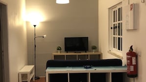 A living room with a TV, a bench, a floor lamp, and a fire extinguisher.