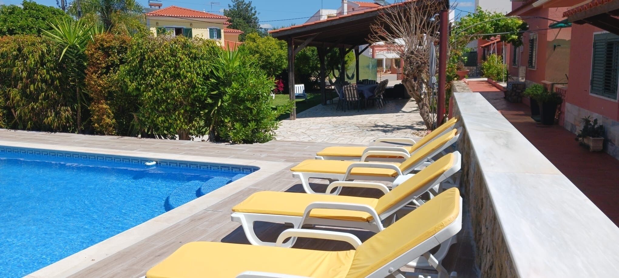 A poolside area with lounge chairs, a clear blue pool, and surrounding greenery.