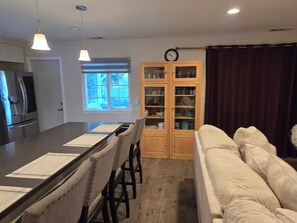 A modern kitchen with a central island, wooden cabinets, and a dining area with a sofa. - Family Fun for all ages!  Military Welcome (San Diego)